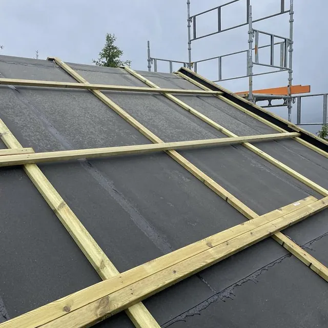 Skråtak med svart undertak og påmonterte lekter, stillas i bakgrunnen.