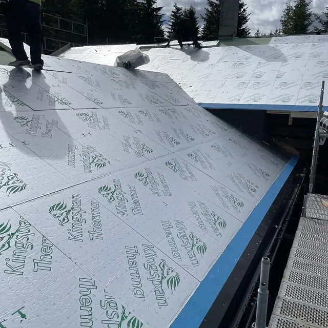 Skråtak dekkes med hvite isolasjonsplater merket “Kingspan Therma”, arbeidere i arbeid.